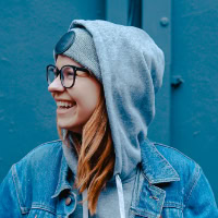 Smiling woman in casual hoodie and glasses, outdoor setting.
